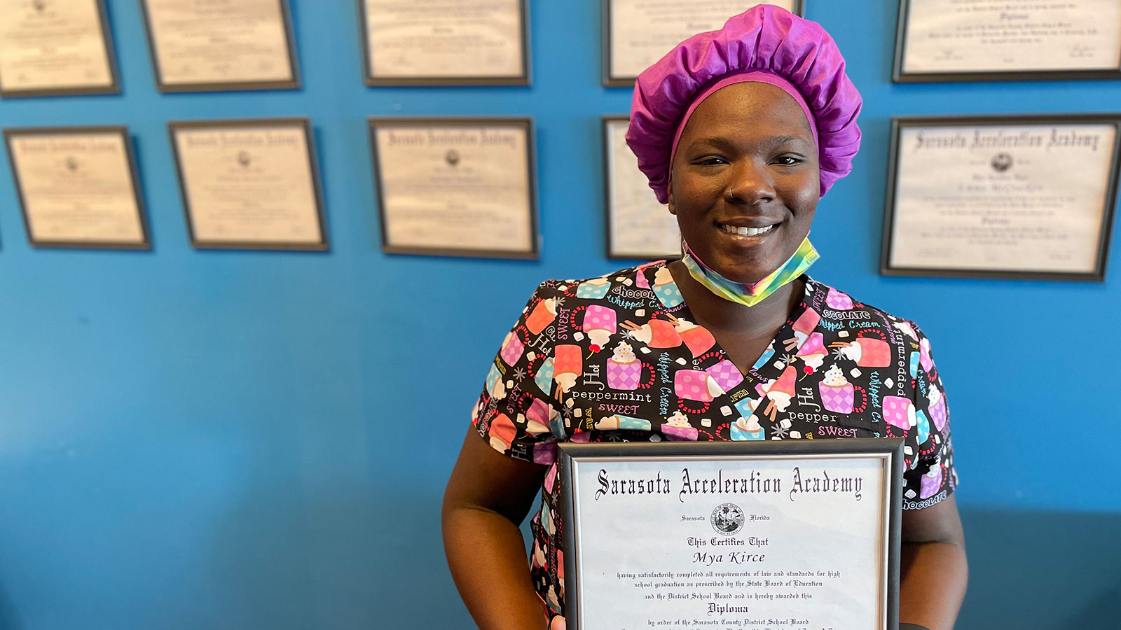 Woman stands smiling and holding a high school diploma