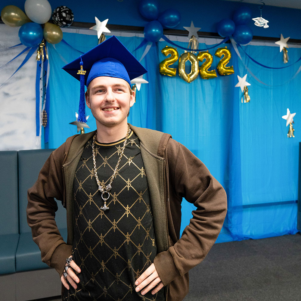 Man stands with hands on his hips wearing a graduation hat.