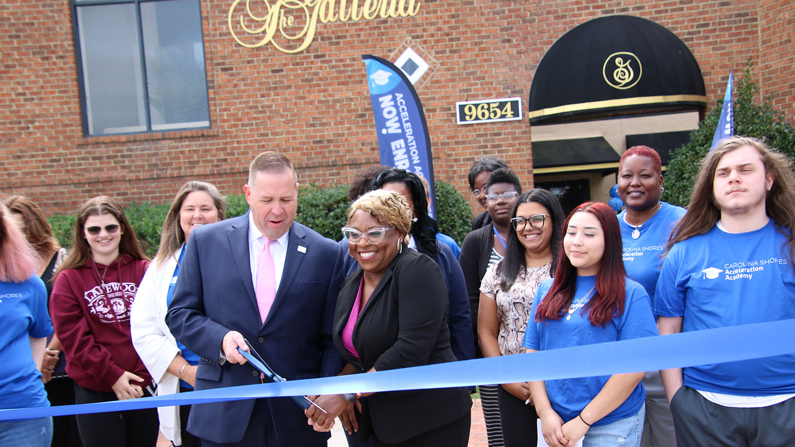 A group of people stand in front of Carolina Shores Acceleration Academy cutting the grand opening ribbon.